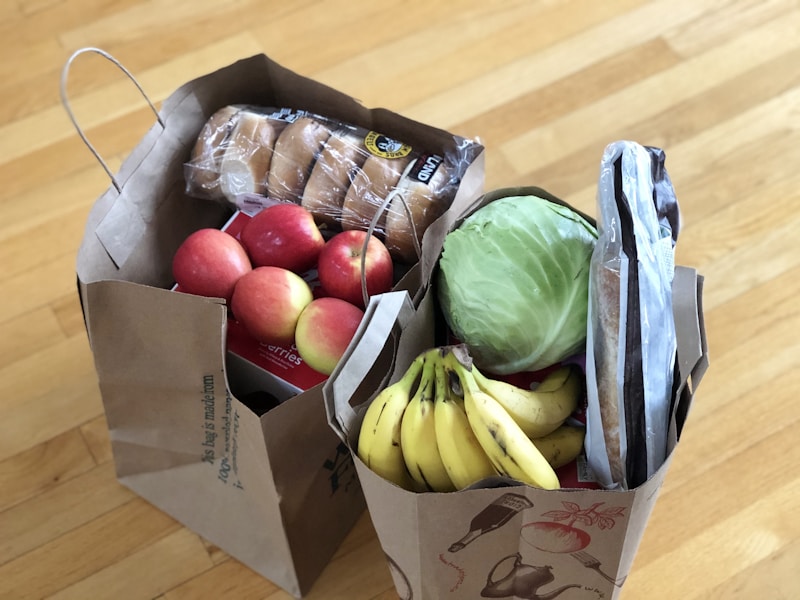 Brown paper grocery bags filled with fresh vegetables, bread, and budget staples.