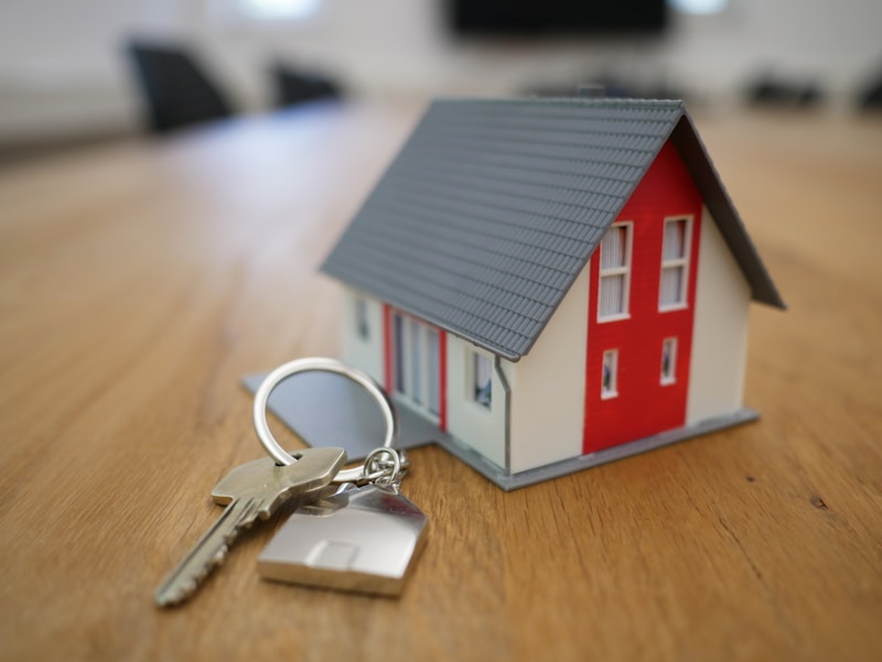 House keys resting on a rustic wooden table in front of a cozy residential home doorway.